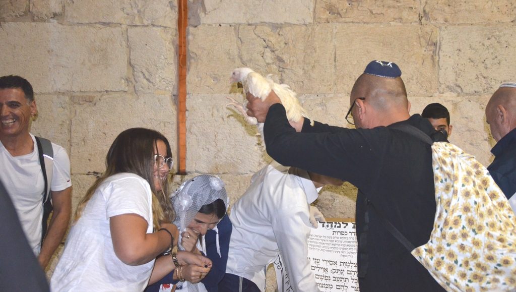 Man waving bird over head of two women for Keporos at Jaffa Gate Jerusalem 