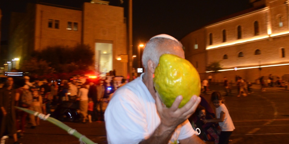 Man holding esrog as big as his head in Jerusalem at night on Sukkot