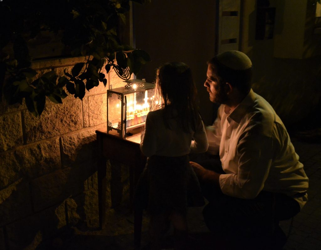 Man and daughter looking at Hanukkah menorah outside